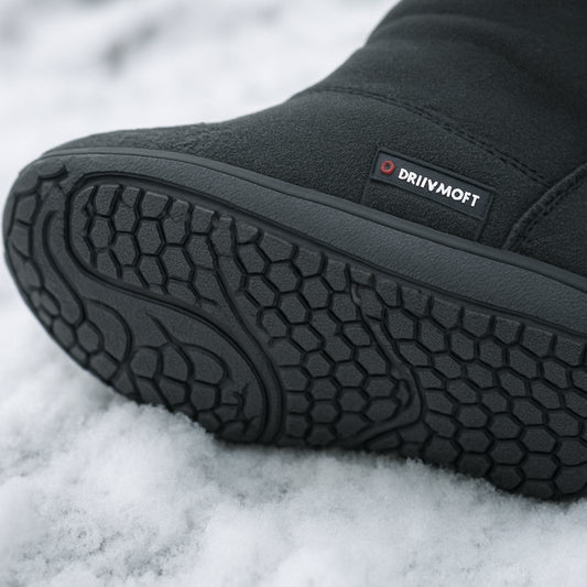 En närbild av en vintervänlig barfotaskosula med Primaloft‑isolering, tydligt synliga mönster och snö på marken. Alt: Vinterbarfotaskor med flexibel sula och tunn isolering för kallt väder.