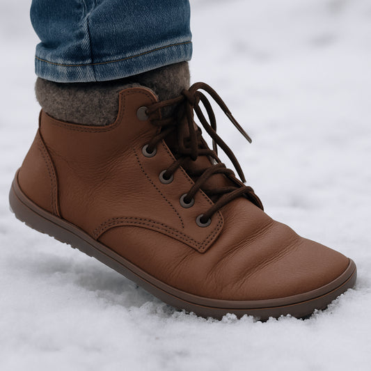 En närbild av en person som provar barfotakängor i snö, med fokus på fotens naturliga rörelse och den tunna sulan. Alt: barfotakängor vinterfottyp